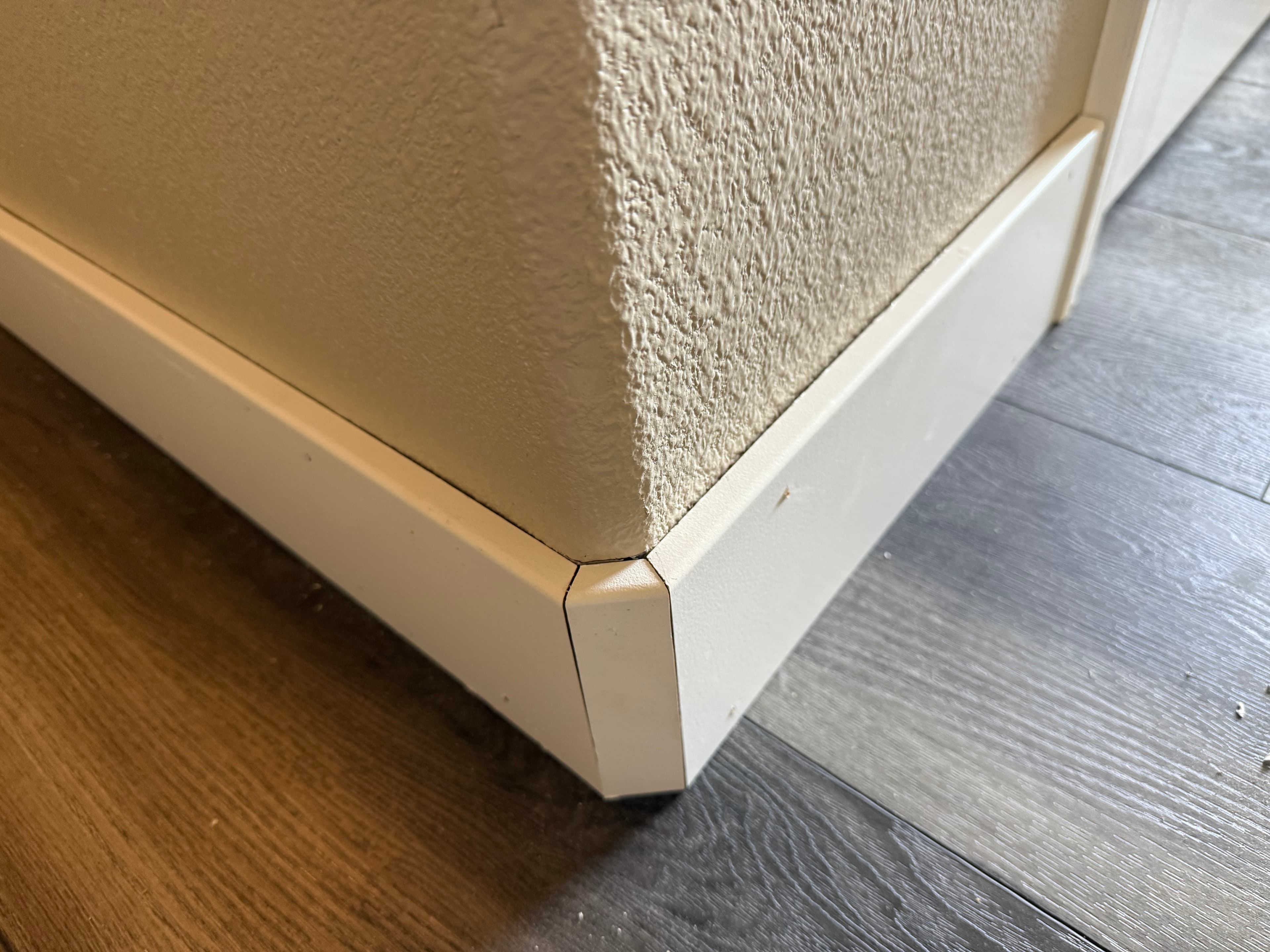 White baseboard bullnose corner joint on a textured wall above wood-look plank flooring.